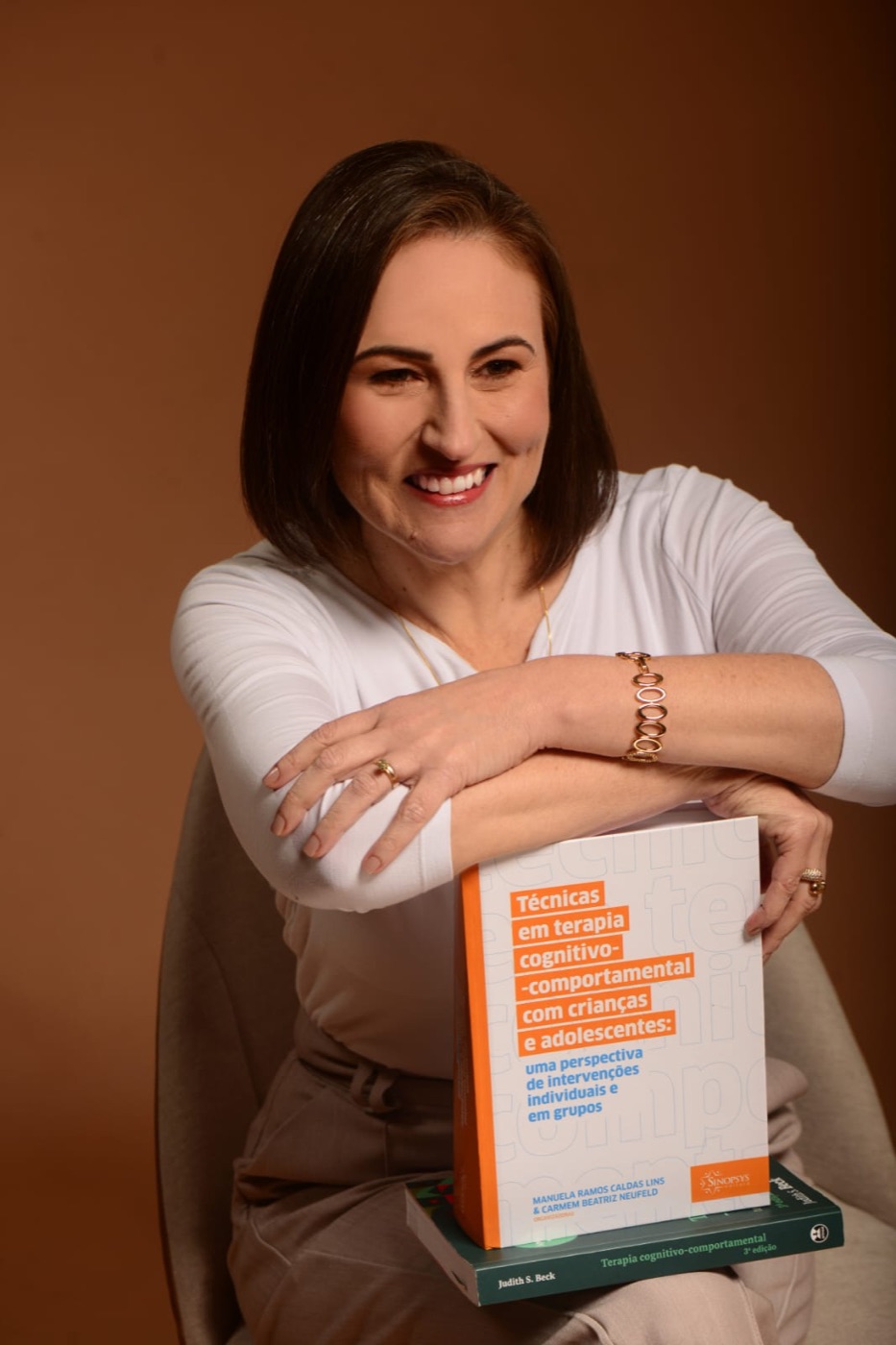 Carla Rizzi sorrindo, apoiada em livros de psicologia
